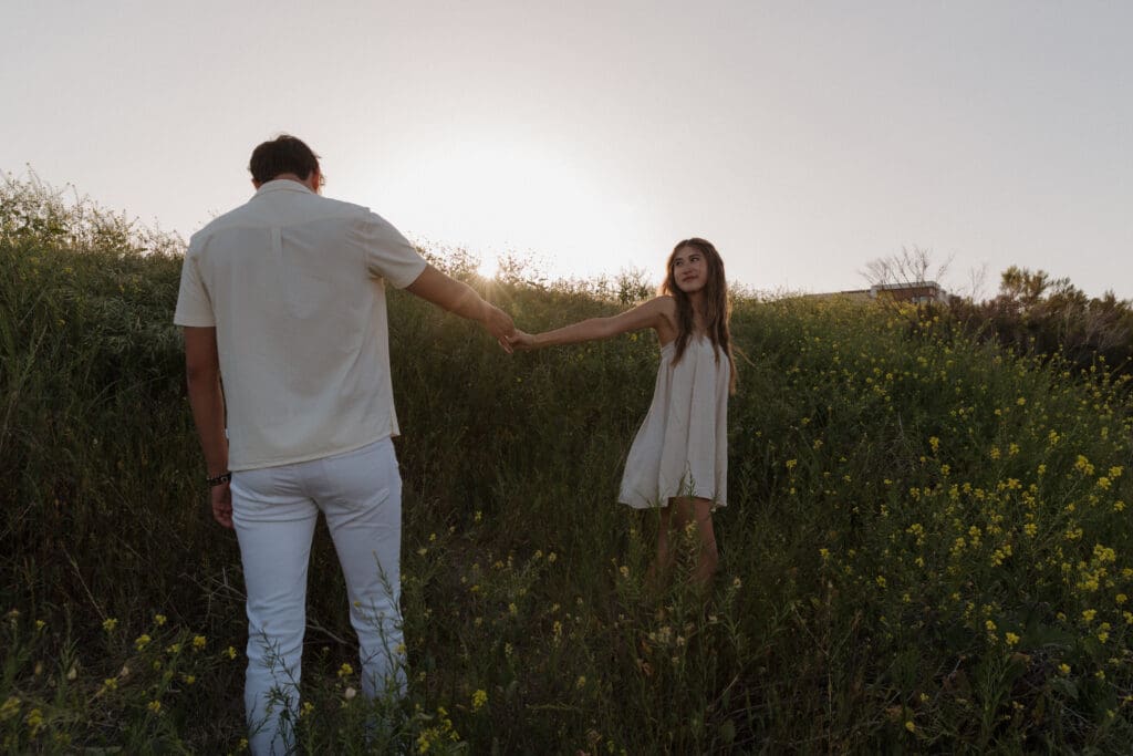 Couple holding hands in a wild-flower field in San Diego.